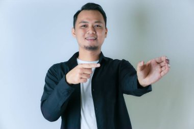 Siyah tişörtlü ve beyaz tişörtlü gülümseyen bir adam açık avucunu işaret ediyor, sanki düz bir arkaplan üzerinde bir şey sunuyor ya da sergiliyor gibi..