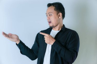 Siyah gömlekli bir adam avucunun içini gösterir. Beyaz arka planda bir şey ima eder ya da gösterir..