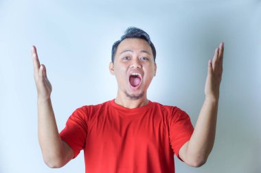 Kırmızı gömlekli bir adam sevinçle yumruklarını kaldırır kutlama jesti olarak, beyaz arka planda geniş bir gülümsemeyle..