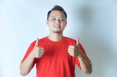 Kırmızı tişörtlü bir adam gülümsüyor ve beyaz bir arka plana karşı olumlu bir hareket ve onay gösteriyor..