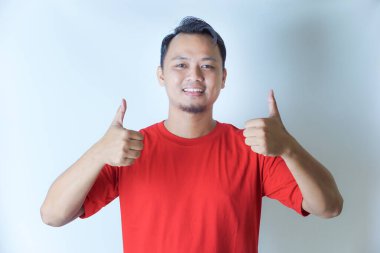 Kırmızı tişörtlü bir adam gülümsüyor ve beyaz bir arka plana karşı olumlu bir hareket ve onay gösteriyor..