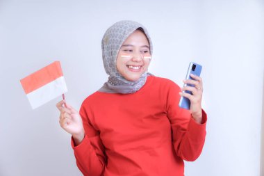 Kırmızı tişörtlü bir kadın elinde Endonezya 'nın Bağımsızlık Günü' nü kutlayan bir bayrak ve akıllı telefon tutarken gülümsüyor..