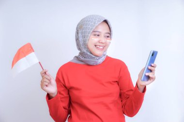 Kırmızı tişörtlü bir kadın elinde Endonezya 'nın Bağımsızlık Günü' nü kutlayan bir bayrak ve akıllı telefon tutarken gülümsüyor..