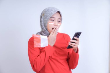 Kırmızı elbiseli bir kadın Endonezya 'nın Bağımsızlık Günü' nü kutlarken elinde bir Endonezya bayrağı tutarken telefonuna bakıyor..