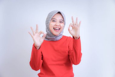 Kırmızı tişörtlü, yüzü boyalı ve tesettürlü neşeli bir kadın bir 'tamam' hareketi gösterir. Endonezya Bağımsızlık Gününü Kutlama.