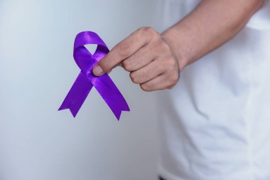 Bir el, aile içi şiddet ve kanser gibi çeşitli nedenler için farkındalığı ve desteği simgeleyen mor bir kurdele tutuyor. Sağlık ve Dünya Kanser Günü konsepti