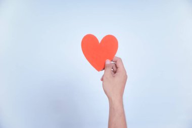 Bir el, temiz, beyaz bir arka plana karşı sevgi ve sevgiyi sembolize eden canlı bir kırmızı kalbi tutar. Dünya Kalp Günü konsepti