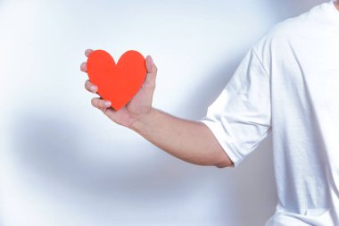 Bir el, temiz, beyaz bir arka plana karşı sevgi ve sevgiyi sembolize eden canlı bir kırmızı kalbi tutar. Dünya Kalp Günü konsepti