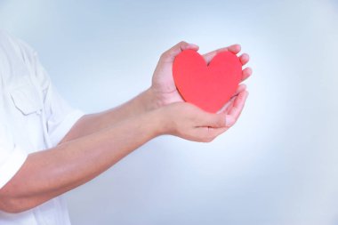 Bir el, temiz, beyaz bir arka plana karşı sevgi ve sevgiyi sembolize eden canlı bir kırmızı kalbi tutar. Dünya Kalp Günü konsepti