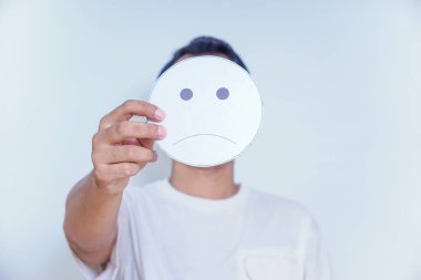 Bir insan üzgün bir yüz sembolü tutar, duyguları ve sıklıkla sakladığımız duyguların karmaşıklığını yansıtır. dünya ruh sağlığı günü konsepti