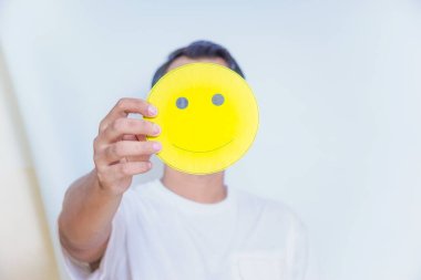 A person holding a cheerful yellow smiley face symbolizes joy and positivity in a bright setting. world mental health day concept