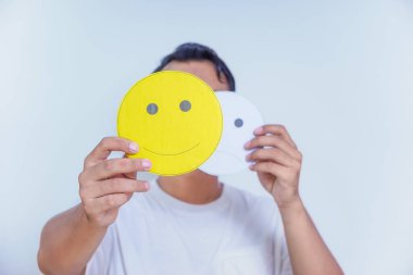 Bir insan iki yüz ifadesi kartı tutar, biri mutlu diğeri tarafsız, duyguları ve tercihleri sembolize eder. dünya ruh sağlığı günü konsepti