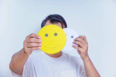 A person holds two facial expression cards, one happy and one neutral, symbolizing emotions and choices. world mental health day concept