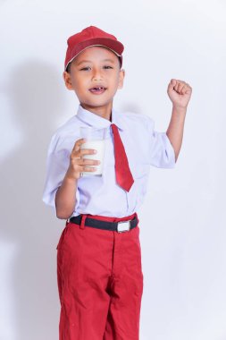 Kırmızı üniformalı neşeli genç bir çocuk elinde bir bardak süt tutuyor, kendine güveni ve neşesi var..