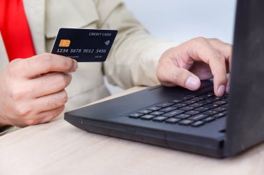 Bir kişi elinde kredi kartı tutarken dizüstü bilgisayar kullanıyor ve online alışveriş yapıyor..