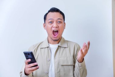 Şaşırmış bir adam akıllı telefonunu elinde tutarken enerjik tepki verir..