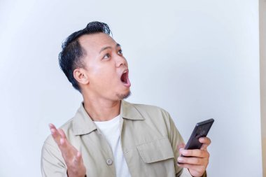 Şaşırmış bir adam akıllı telefonunu elinde tutarken enerjik tepki verir..