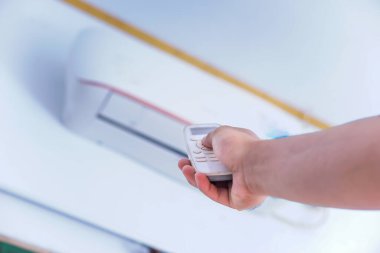 Duvara monte edilmiş klimayı ayarlamak için uzaktan kumanda kullanan biri..