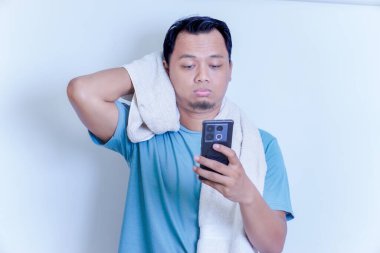 Akıllı telefonu ve havlusunu omzunda tutarken hayal kırıklığına uğramış bir Asyalı.