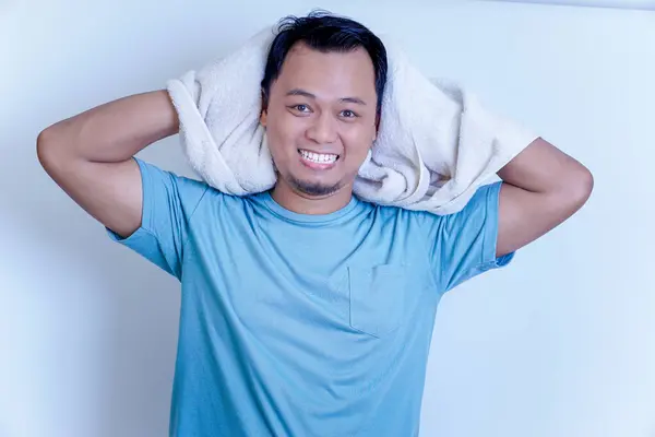 Duştan sonra gülümseyen genç bir Asyalı adam, parlak bir ortamda omzunun üzerinde bir havlu tutuyor..