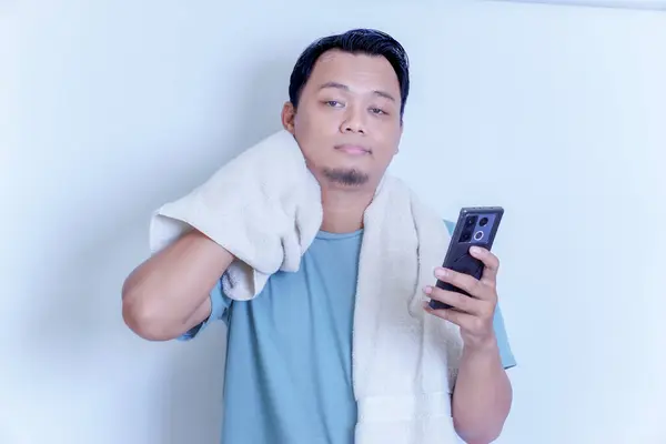 Akıllı telefonu ve havlusunu omzunda tutarken hayal kırıklığına uğramış bir Asyalı.