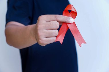 Kırmızı kurdele tutan bir kişi, sağlık sorunları için farkındalığı ve desteği simgeliyor.