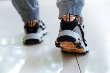 Parlak fayanslar üzerinde yürüyen şık spor ayakkabılar ve rahat pantolonlar giyen bir insan..