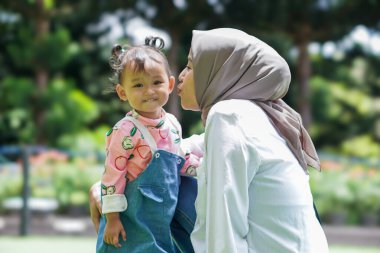 Neşeli Asyalı Müslüman bir kadın ve çocuğu canlı bir bahçede bir anı paylaşıyorlar..