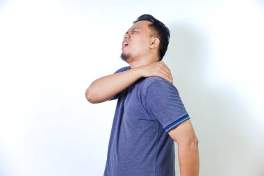 Asyalı bir adam rahatsızlık yaşıyor, omzunu tutuyor ve acı belirtileri gösteriyor..