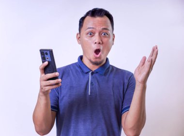 Şaşırmış Asyalı bir adam akıllı telefon tutuyor, ağzı açık şok ya da heyecan ifade ediyor.