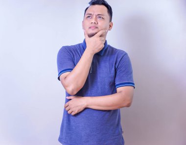 Mavi polo tişörtlü düşünceli bir Asyalı. Düşünceli bir ifadeyle bir fikir üzerinde kafa yoruyor..