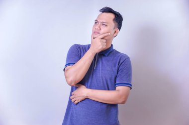 Mavi polo tişörtlü düşünceli bir Asyalı. Düşünceli bir ifadeyle bir fikir üzerinde kafa yoruyor..