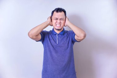 Asyalı bir adam, gürültüyü engellemek için kulaklarını tıkayarak huzursuzluk içinde yüzünü buruşturur..