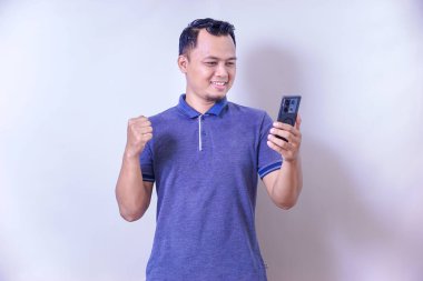 Asyalı bir adam gülümser ve akıllı telefonuyla heyecan verici bir şeyi kontrol ederken kutlama yapar..