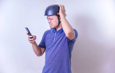 Miğferli Asyalı bir adam akıllı telefonunu kullanırken sinirli görünür..