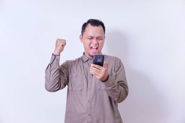 Asyalı bir adam mutlu bir şekilde telefonunu kontrol ediyor, neşeli bir anı yumruğuyla kutluyor..