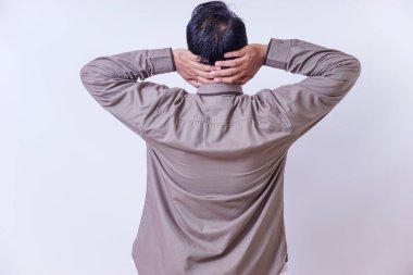 Asyalı bir adam, elleri başının arkasında, gri uzun kollu bir gömlek giyiyor..