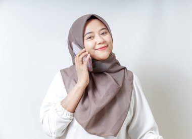 Tesettürlü, tesettürlü gülümseyen Asyalı bir kadın beyaz arka planda izole edilmiş neşeli bir tavır sergiliyor.