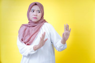 Tesettürlü Asyalı bir kadın, parlak sarı bir arka plana karşı kendini savunur.