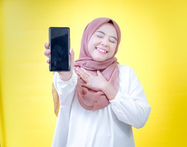 Neşeli Asyalı bir kadın, parlak sarı bir arka planda mutlulukla ışıldayan akıllı bir telefon tutuyor..