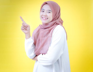 Tesettürlü neşeli Asyalı bir kadın yukarı bakıyor, parlak sarı bir arkaplana karşı..