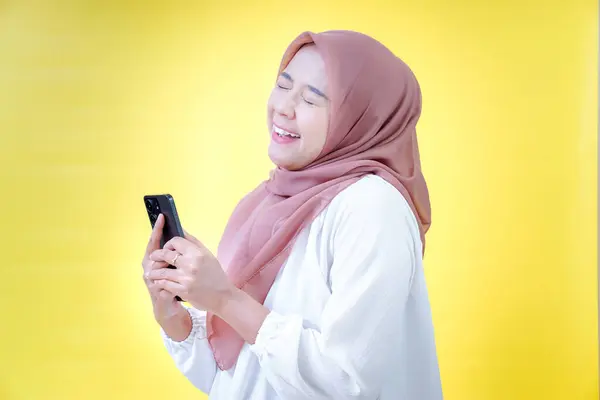 Gülümseyen Asyalı bir kadın akıllı bir telefon tutuyor, tesettüre bürünüyor ve gülümsüyor.