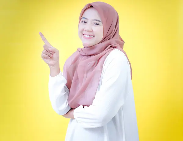 Tesettürlü neşeli Asyalı bir kadın yukarı bakıyor, parlak sarı bir arkaplana karşı..