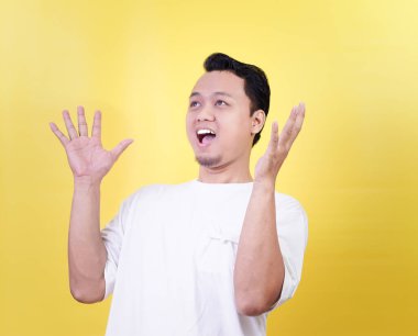 Genç Asyalı bir adam, parlak sarı bir arka plana karşı heyecanını dile getiriyor..