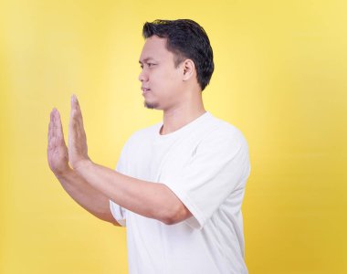 Asyalı bir adam parlak sarı bir arka planda durmak ya da itmek için işaret eder..