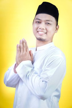 Asyalı Müslüman adam el sallama hareketiyle birine gülümsüyor.