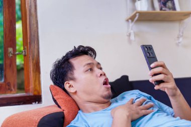 Şaşırmış Asyalı bir adam telefonundan bir şey izlerken bir şok anını yakalıyor..