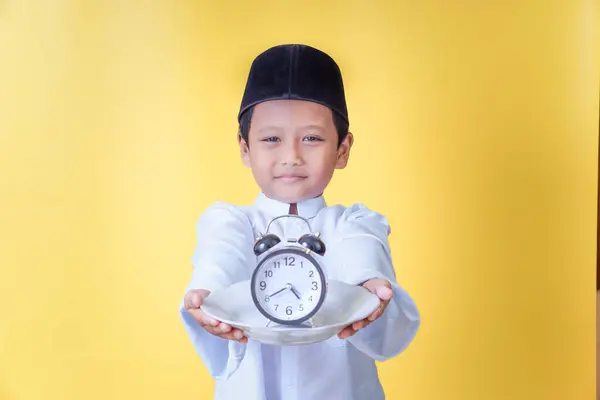 Geleneksel Müslüman kıyafetli bir Asyalı çocuk, sahur ya da iftarı simgeleyen bir saati tabakta sunuyor..