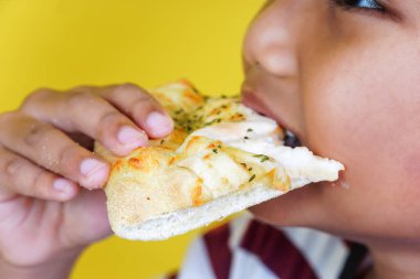 A child eagerly bites into a cheesy slice of pizza, enjoying a delicious moment. international foods day concept clipart