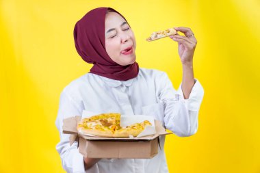 Neşeli Asyalı bir kadın pizzanın tadını çıkarıyor. Parlak sarı bir zemin üzerinde. Yemek aşkını gösteriyor..